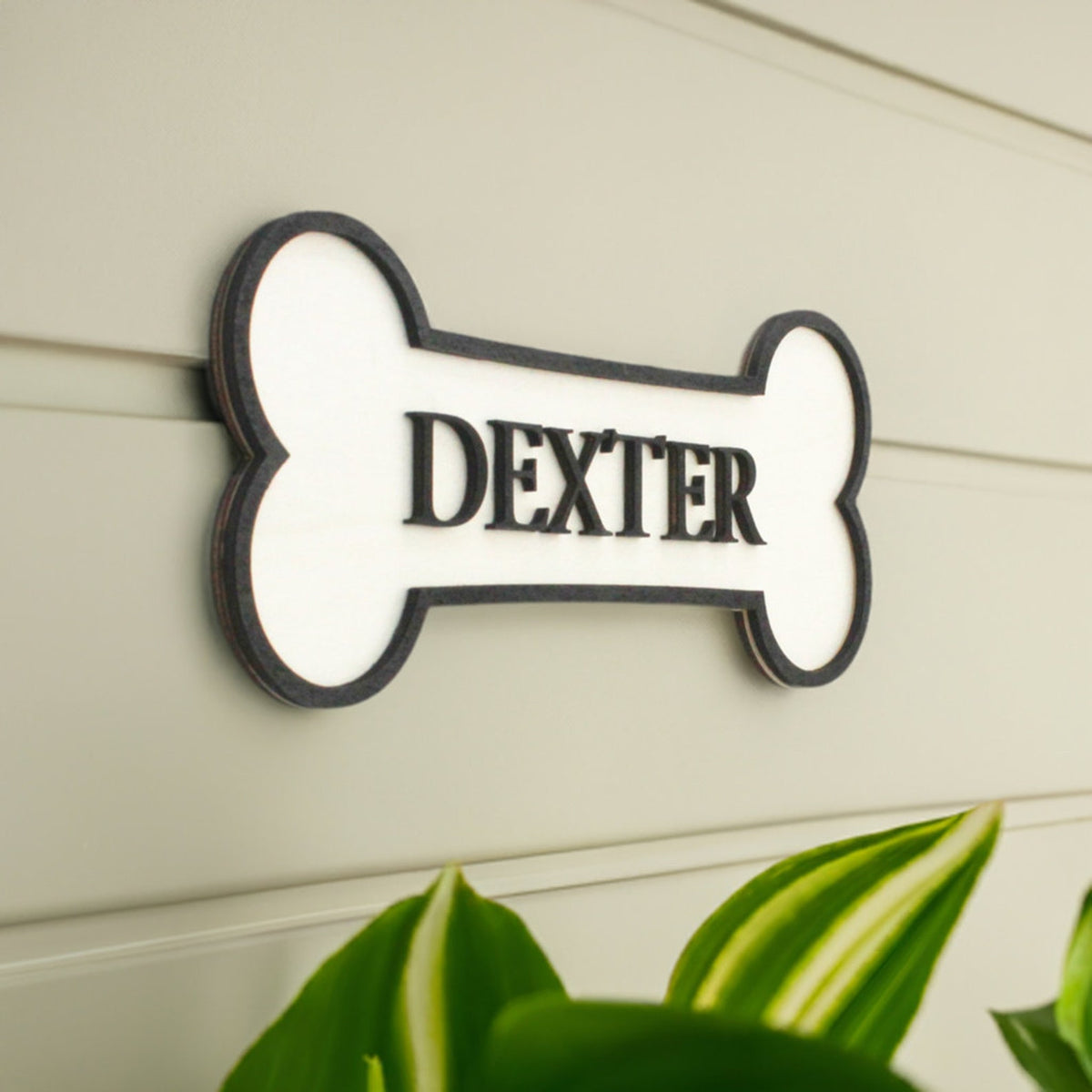 Personalised Dog's Name Wall Sign Shaped as a Bone, with Raised Wooden Wording in Black against wooden background, Pet Gift